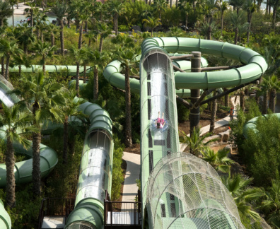 A woman is gliding on a green enclosed slide, the unenclosed part has a net for safety